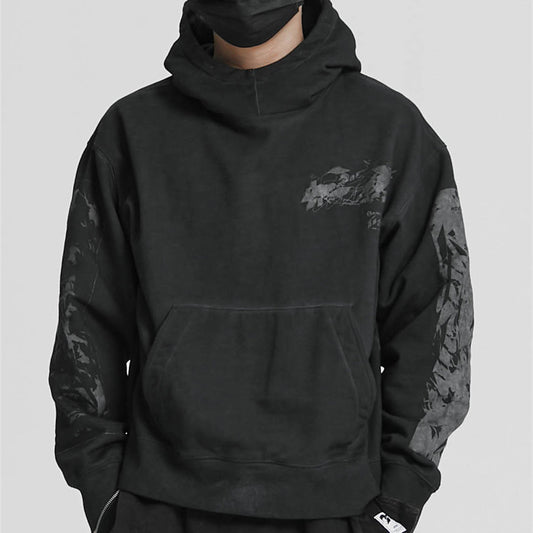 Man wearing an oversized black streetwear hoodie with subtle tonal graphics on the chest and sleeves and 
a front pouch pocket. 