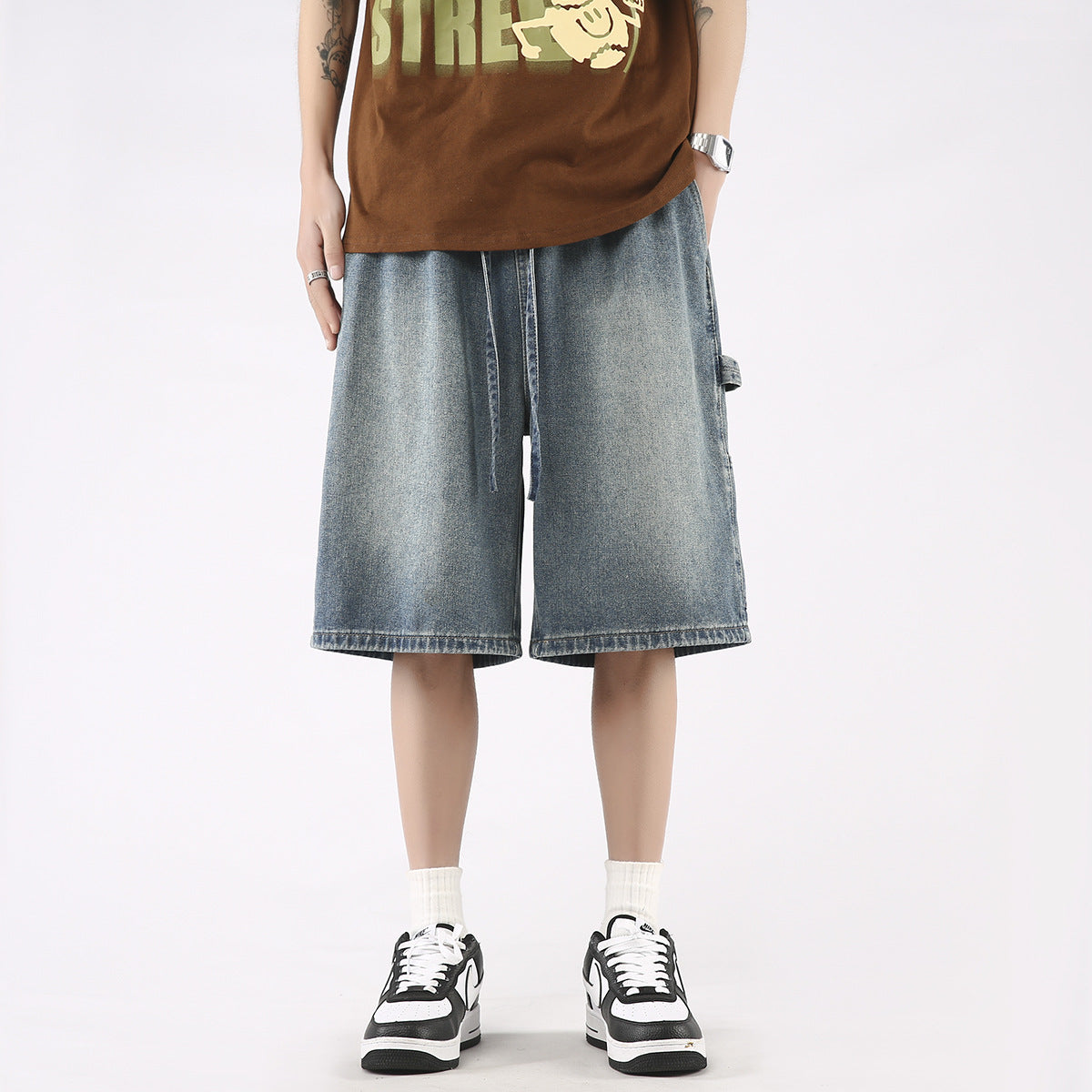 Man wearing loose fit washed denim knee-length shorts with white socks and black sneakers.