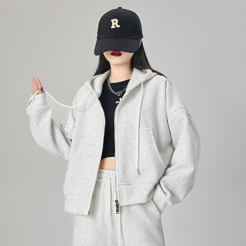 Woman wearing an ivory oversized zip-up hoodie with hood and front pockets, styled with ivory baseball cap 
and joggers, brown crop top. 