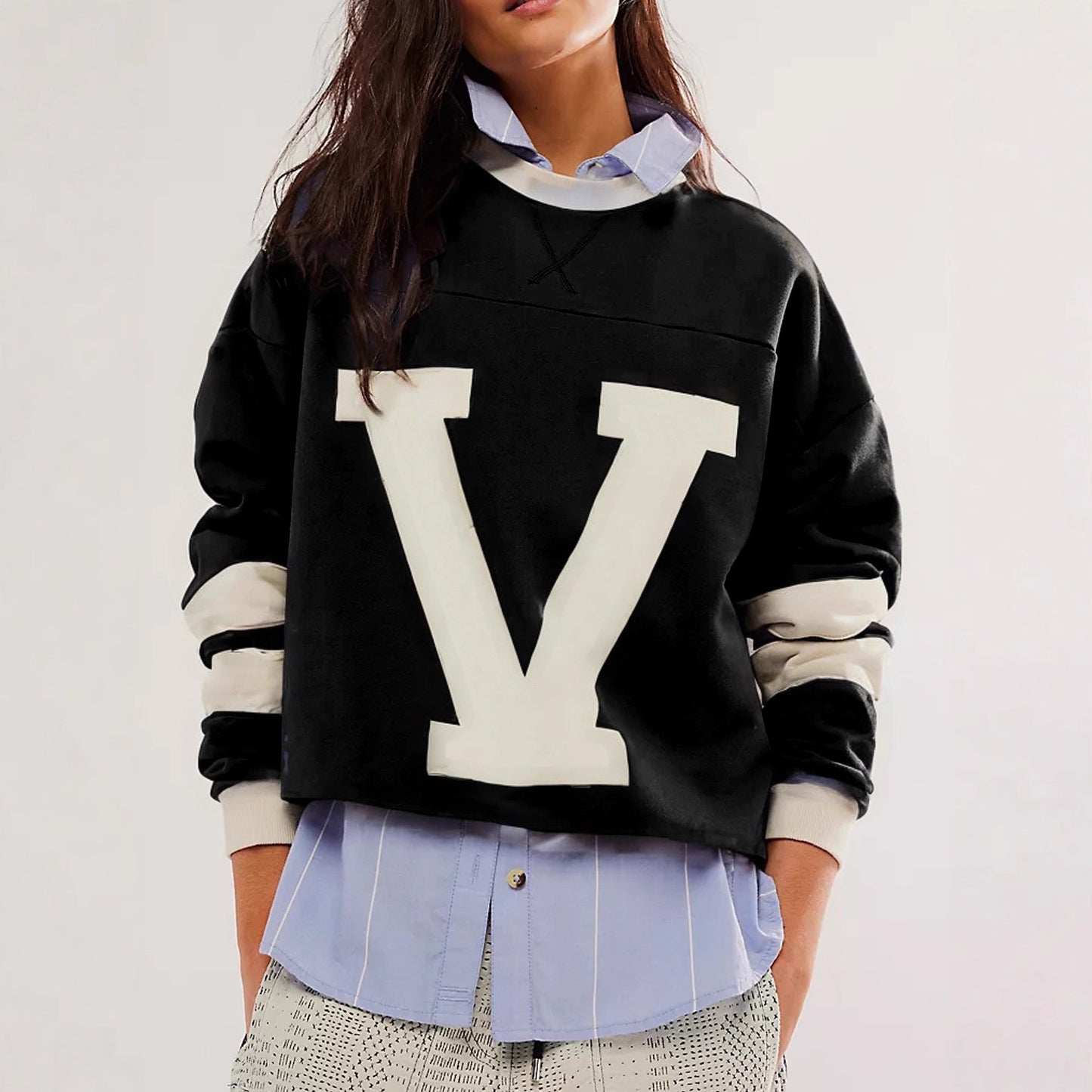 Woman wearing an oversized navy blue sweatshirt with white letter graphic and striped sleeves in varsity 
style design. 