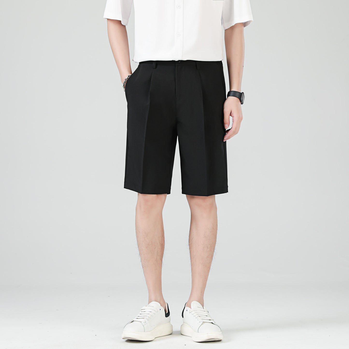 Man wearing beige tailored knee-length shorts styled with a black shirt and white sneakers.
