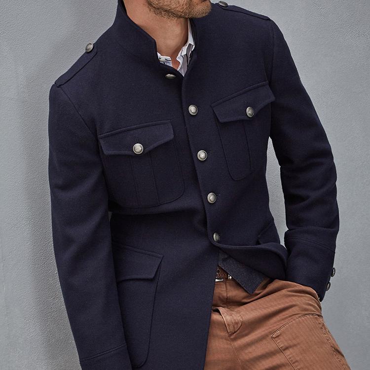 Man wearing a navy blue military-style jacket with stand collar and buttoned flap pockets.
