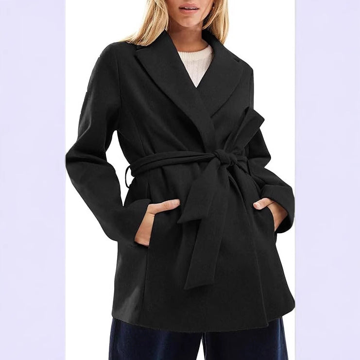Woman wearing a black belted wrap coat with notched collar and side pockets.