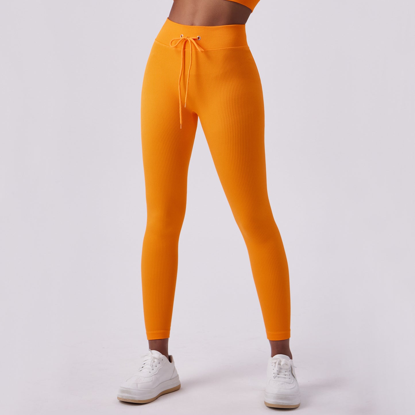 Woman wearing high-waisted ribbed orange leggings with adjustable drawstring waistband and white 
sneakers.