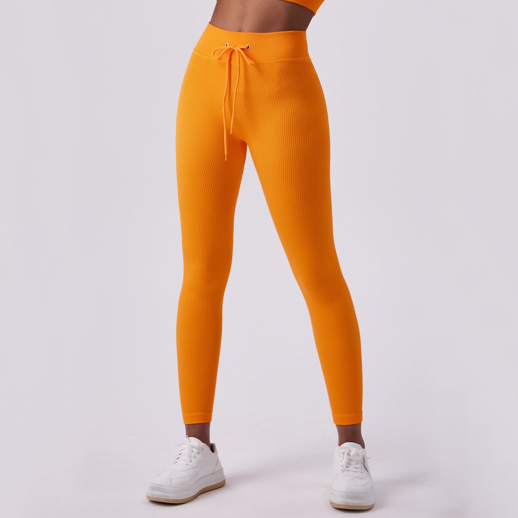 Woman wearing high-waisted ribbed orange leggings with adjustable drawstring waistband and white 
sneakers.