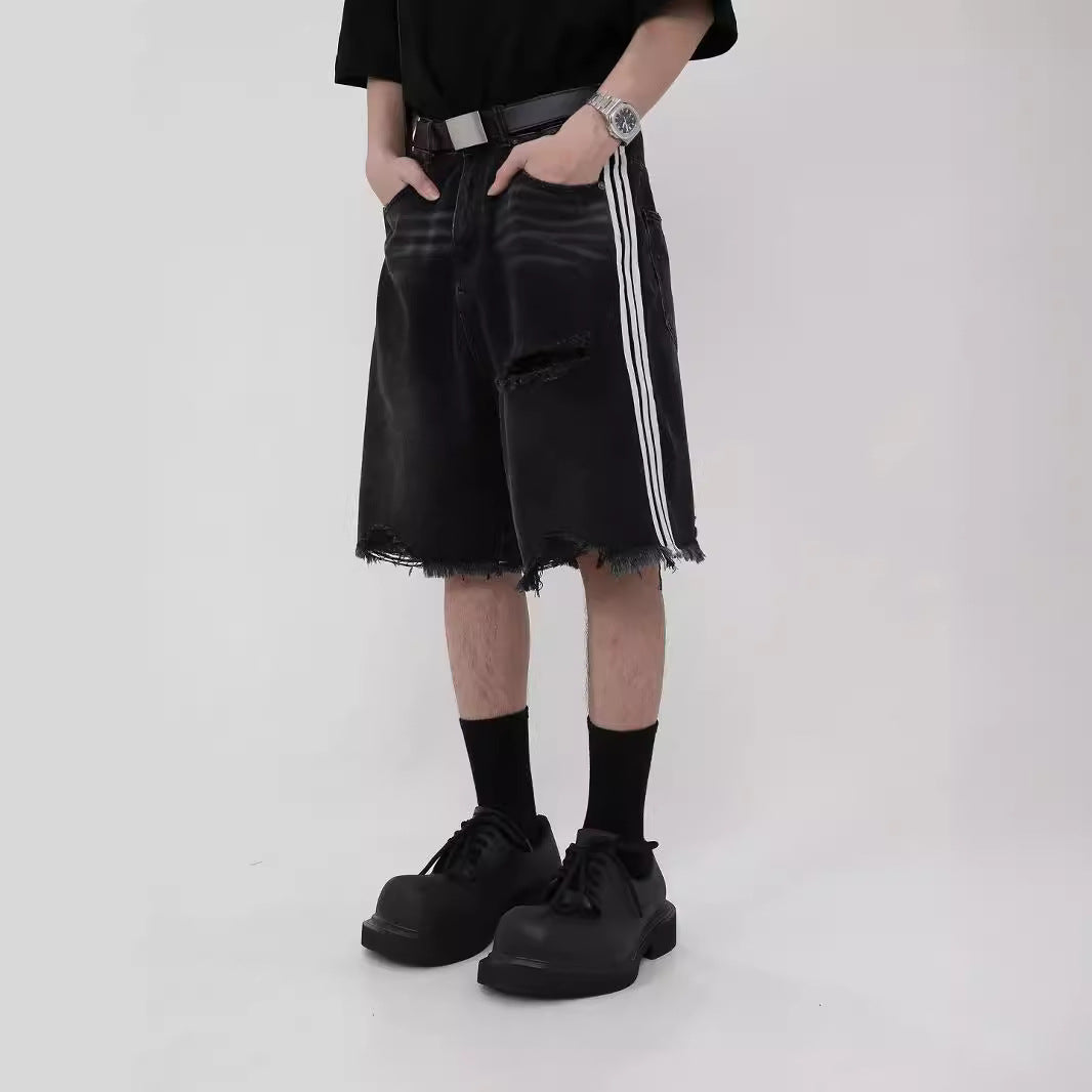 Man wearing black distressed loose-fit denim shorts with white side stripes, black socks, and chunky black 
shoes. 