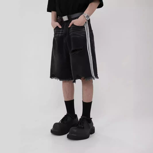 Man wearing black distressed loose-fit denim shorts with white side stripes, black socks, and chunky black 
shoes. 