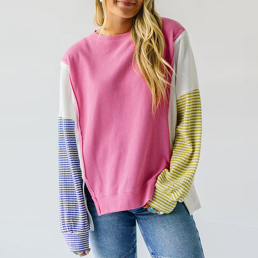 Woman wearing a pink colorblock oversized crewneck sweatshirt with contrasting striped sleeves styled with 
blue jeans. 