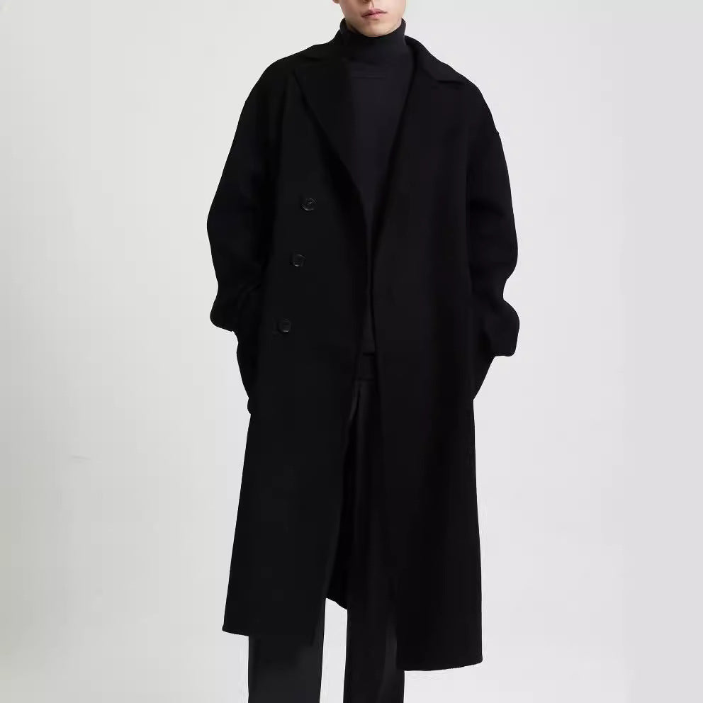 Man wearing a long black overcoat layered over a black turtleneck. 