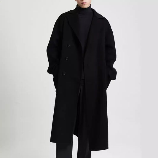 Man wearing a long black overcoat layered over a black turtleneck. 