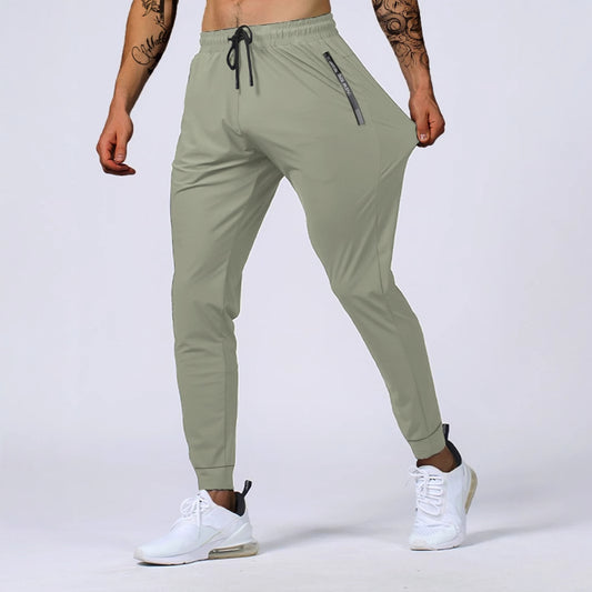 Man wearing light green nylon athletic jogger pants with elastic waistband, zippered pocket, and white 
sneakers.