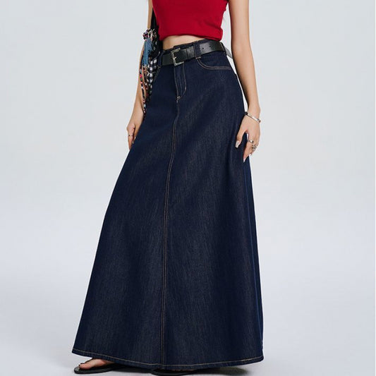 Woman wearing a high-waisted dark blue denim maxi skirt with A-line silhouette and belt, styled with a red 
top and a purse. 
